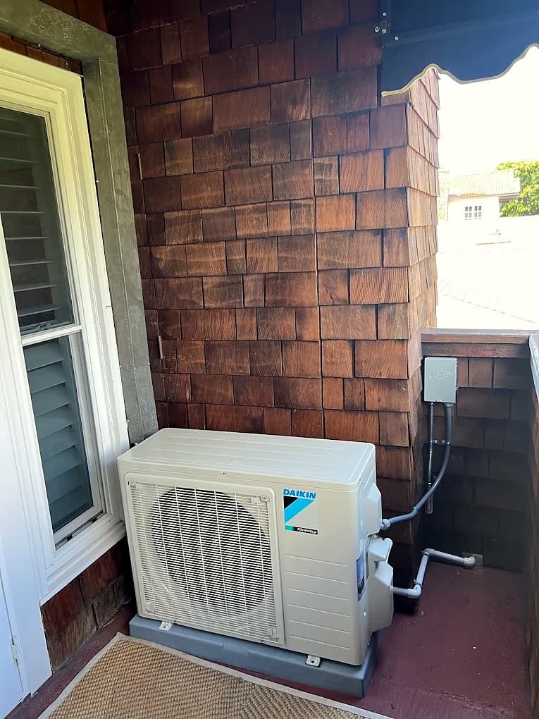 Daikin mini-split outdoor unit beside a shingled wall